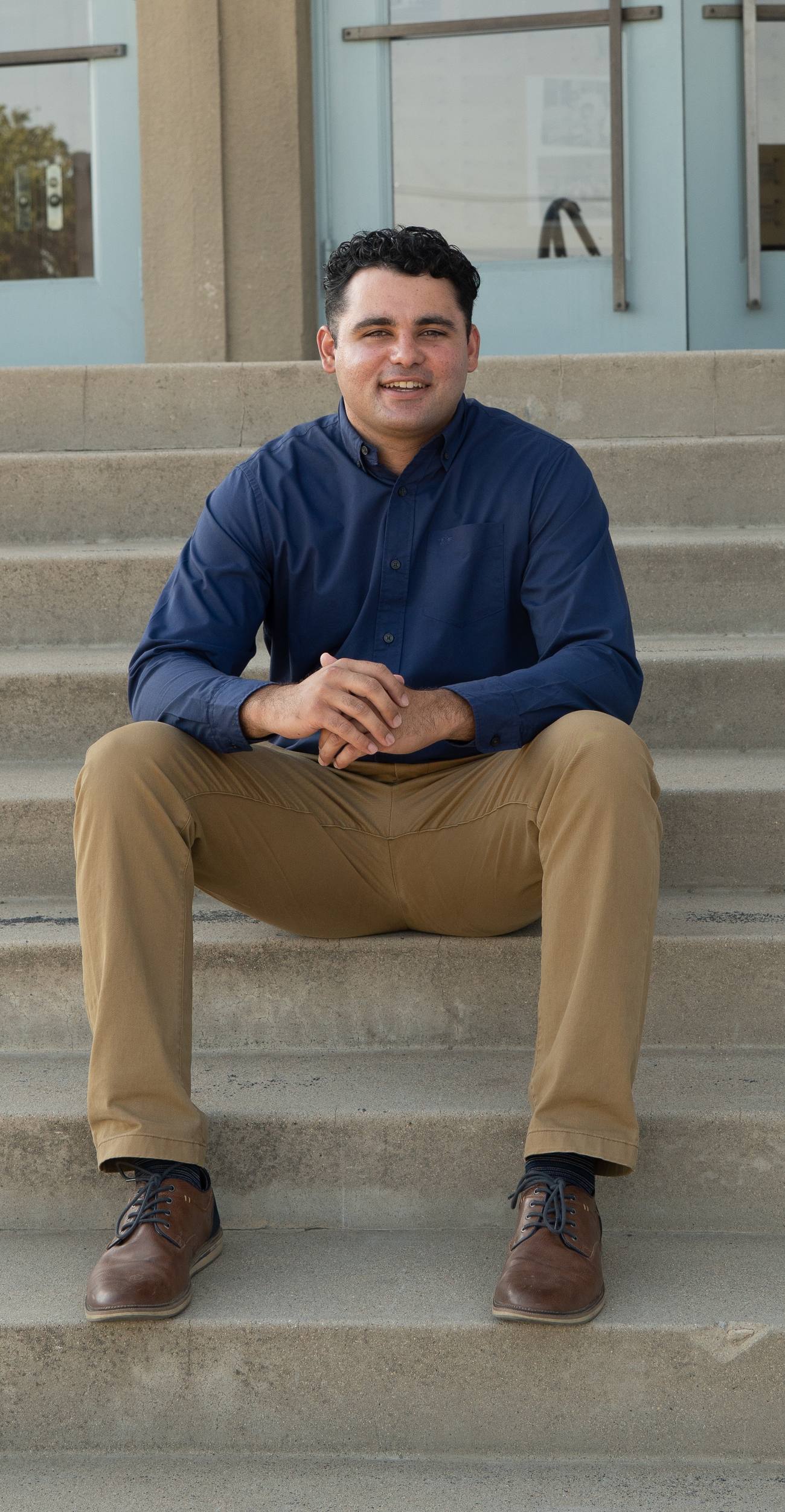 Dylan Pearson smiling, sitting on the steps of a Bakersfield City School District building